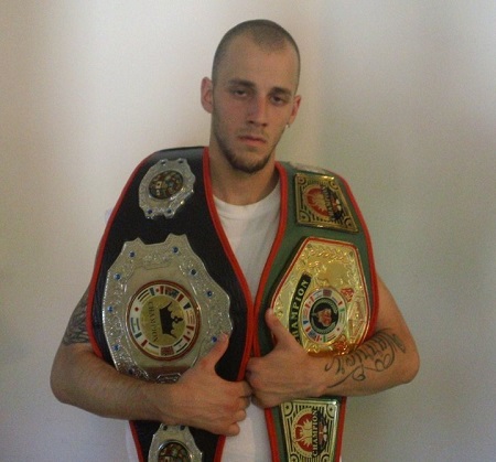 Charlie with two fake boxing belts on his shoulders clutching them.